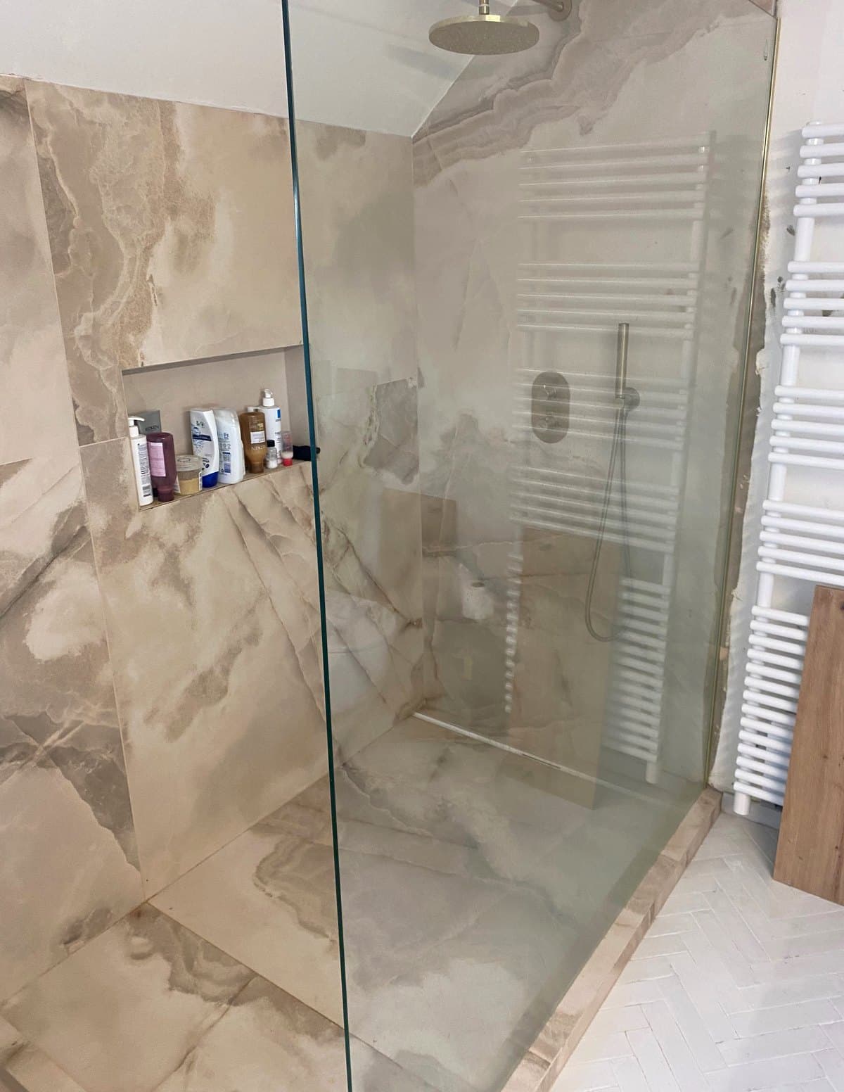 Douche à l'italienne en grès cérame effet onyx avec paroi en verre et ciel de pluie en laiton brossé
